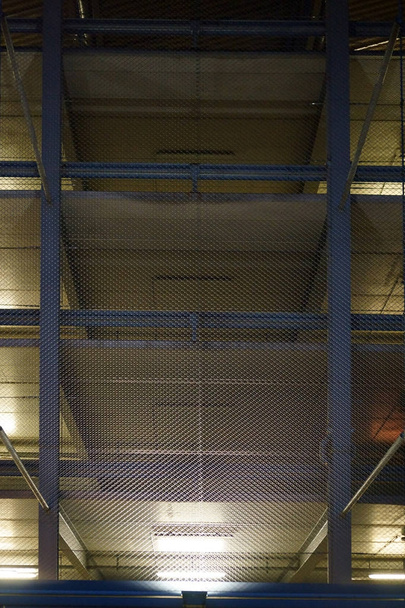 Oświetlony parking w garażu w nocy / otwarty garaż z kilku parking wielopoziomowy chroniony przez drutu siatki jest oświetlony w nocy.                          - Zdjęcie, obraz