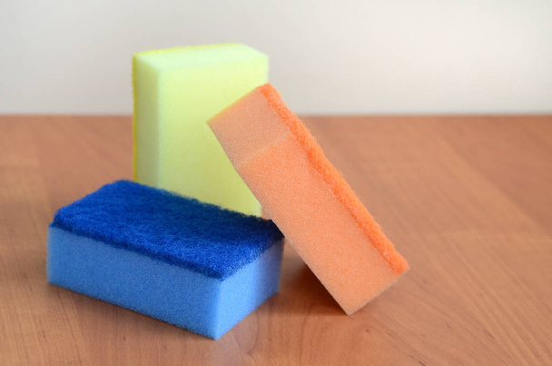 A few kitchen sponges lie on a wooden kitchen countertop. Colorful objects for washing dishes and cleaning in the house are ready for use - Foto, afbeelding