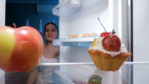 4k footage of young woman taking sweet cake from refrigerator at night - Záběry, video