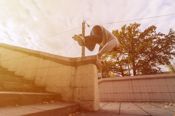 A young guy performs a jump through the concrete parapet. The athlete practices parkour, training in street conditions. The concept of sports subcultures among youth - Photo, Image