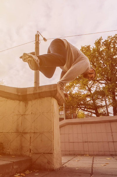 Молодой парень совершает прыжок через бетонный парапет. Спортсмен практикует паркур, тренируется в уличных условиях. Концепция спортивных субкультур среди молодежи
 - Фото, изображение