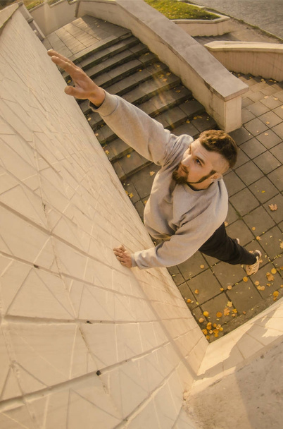 A young guy overcomes obstacles, climbing on concrete walls. The athlete practices parkour, training in street conditions. The concept of sports subcultures among youth - Photo, Image