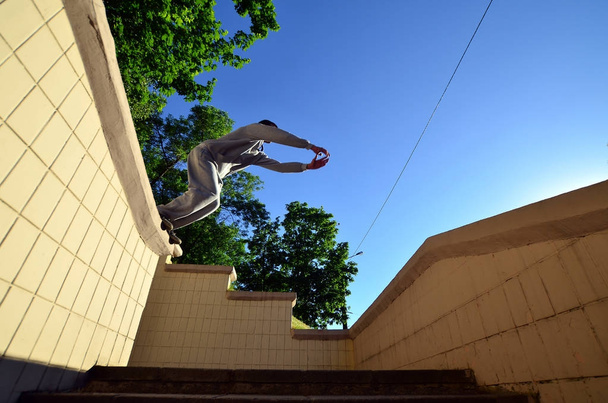 Nuori mies tekee hypyn betonikaistaleiden väliin. Urheilija harjoittelee parkour, koulutusta kadun olosuhteissa. Alareuna
 - Valokuva, kuva