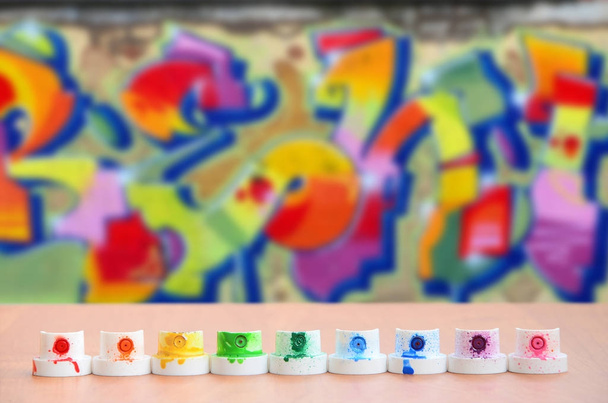 Грязные разноцветные форсунки от распылителя краски выстроены на деревянном столе на фоне цветного граффити в диком стиле. Концепция уличного искусства
 - Фото, изображение