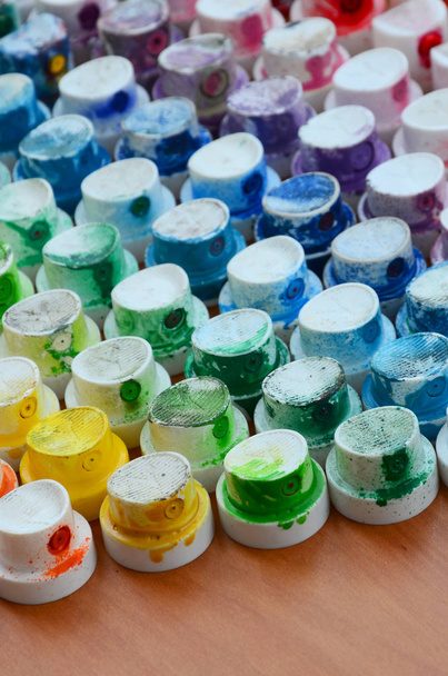 Ένα πρότυπο από μια πολλά ακροφύσια από ψεκασμού βαφής για κατάρτιση γκράφιτι, αλείφεται σε διαφορετικά χρώματα. Τα πλαστικά καπάκια που διοργανώνονται σε πολλές σειρές σχηματίζοντας το χρώμα του ουράνιου τόξου - Φωτογραφία, εικόνα