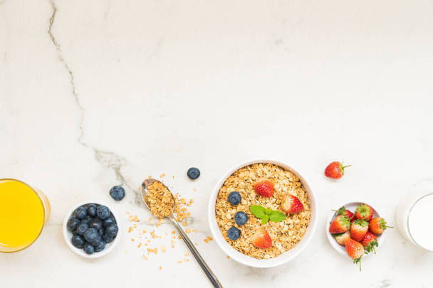 健康的な朝食は、白い石のテーブル背景にブルーベリーとイチゴとブラック コーヒー、牛乳、オレンジ ジュースとグラノーラを設定 - 写真・画像