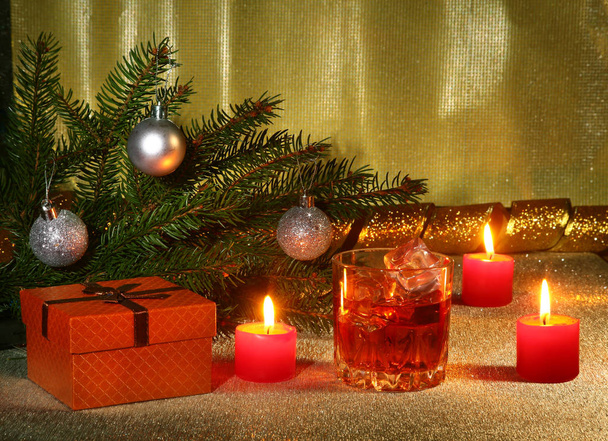 christmas decoration with glass of whiskey or cognac, christmas candles, tree and gift box on a sparkling background. New Year decoration. - Foto, Imagem