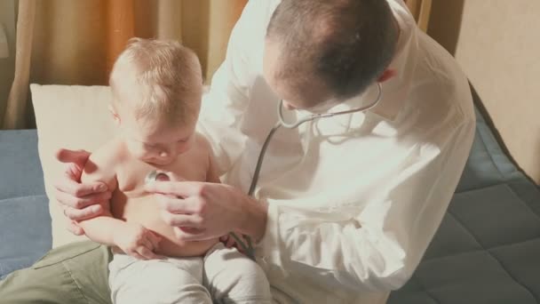 The doctor visits the baby patient at home. Baby with stethoscope - Кадри, відео