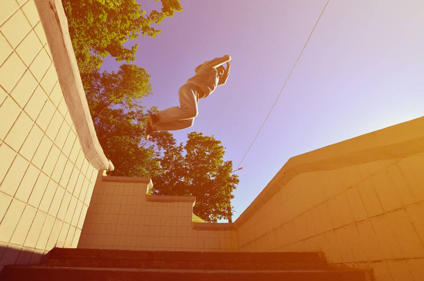 Mladý muž provádí skok přes prostor mezi betonové parapety. Atlet praktiky parkour, školení v ulici podmínkách. Pohled zdola - Fotografie, Obrázek