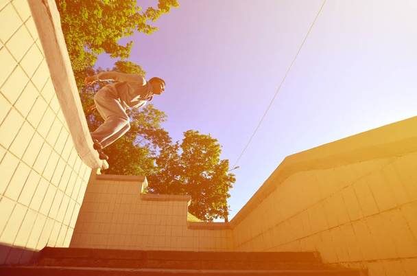 Молодой парень совершает прыжок через пространство между бетонными парапетами. Спортсмен практикует паркур, тренируется в уличных условиях. Нижний вид
 - Фото, изображение
