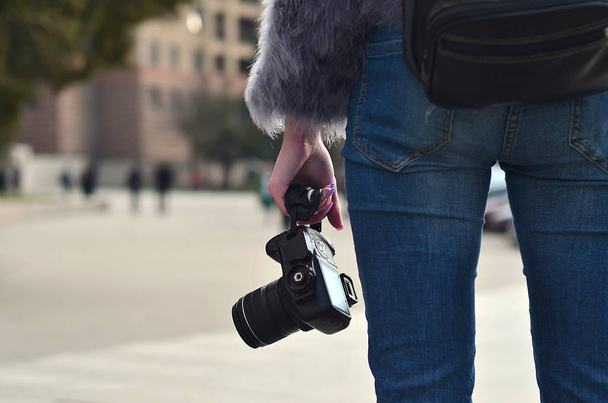 Vista posteriore di una fotografa donna con una moderna fotocamera reflex in mano contro una strada affollata sfocata
 - Foto, immagini