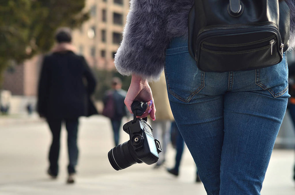 Pohled zezadu na ženské fotografa s černým moderní digitální fotokamery v ruce proti rozostřeného pozadí přelidněné ulici s mnoha lidmi - Fotografie, Obrázek