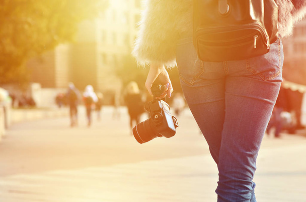 Visão traseira de uma fotógrafa com uma câmera SLR moderna na mão contra uma rua turva lotada
 - Foto, Imagem