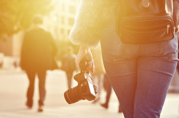 Задний вид женщины-фотографа с черной современной цифровой фотокамерой в руке на размытом фоне переполненной улицы со многими людьми
 - Фото, изображение