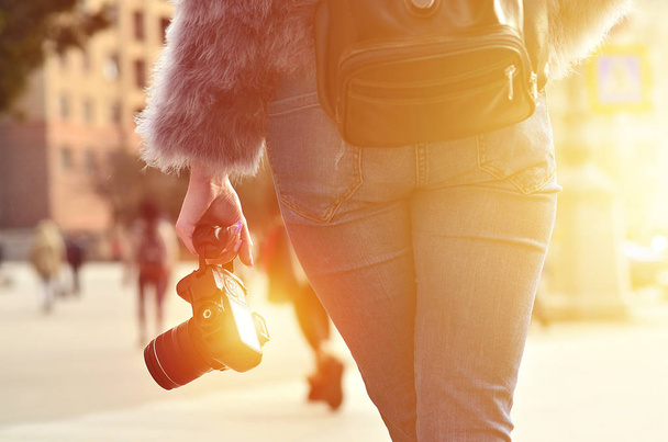 Rear view of a female photographer with a black modern digital photocamera in her hand against a blurred background of crowded street with many people - Foto, immagini