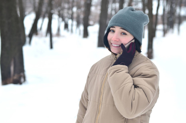 Porträt einer hübschen kaukasischen gepiercten Hipsterin im Winterpark. Sie spricht auf einem modernen Smartphone. Jugend-Straßenmode. Winterspaß. Spaziergänge im Freien. - Foto, Bild