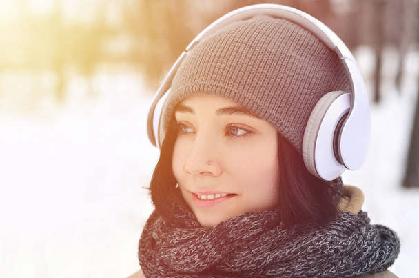 Pretty young girl wear warm winter earmuffs and scarf. Fun brunette female model walk outside with headphones in cold weather. Smiling happy model posing. Good holiday weather - Fotoğraf, Görsel