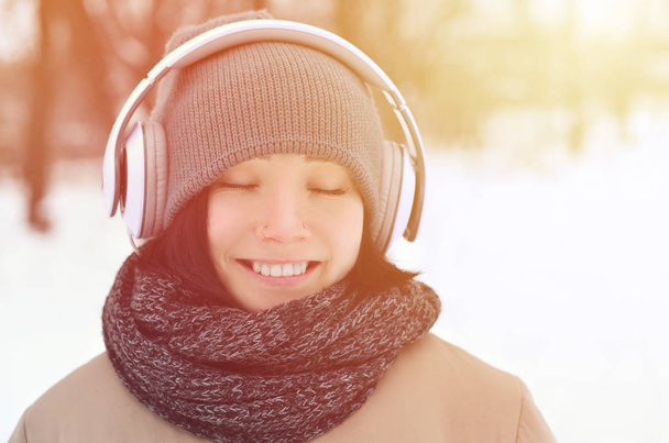 Oldukça çekici beyaz gözlü kız hipster kış park portresi. Kulaklıklar üzerinde müzik dinliyor. Gençlik sokak moda. Kış eğlence. - Fotoğraf, Görsel