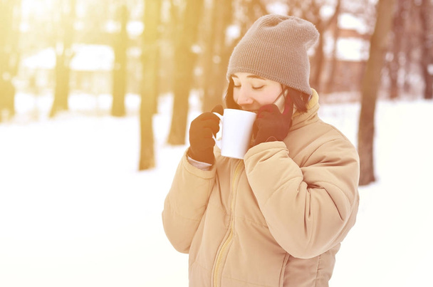 Porträt einer hübschen kaukasischen gepiercten Hipsterin im Winterpark. Sie spricht auf einem modernen Smartphone und trinkt Kaffee. Jugend-Straßenmode. Spaziergänge im Freien. - Foto, Bild