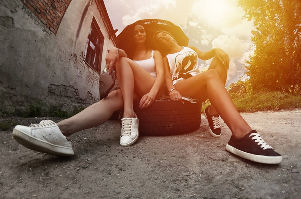 Two young and sexy caucasian girls (blonde and brunette) with wheel wrenches around a big silvery off-road car with an open hood. The concept of repair and maintenance of a car - Photo, Image