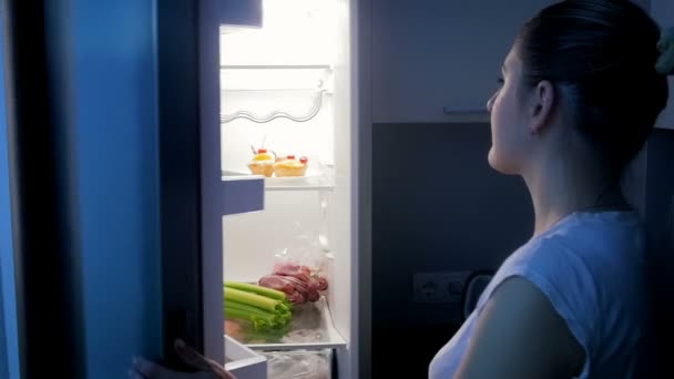 Mujer joven en pijama saca del refrigerador y come manzana por la noche
 - Metraje, vídeo