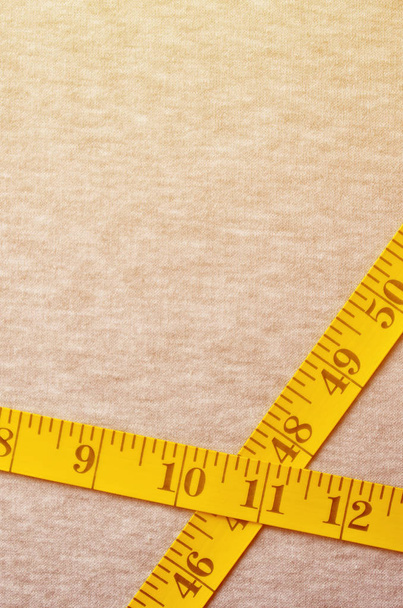 The measuring tape of yellow color with numerical indicators in the form of centimeters or inches lies on a gray knitted fabric. Background concept for sewing clothes for specific body sizes - Photo, Image