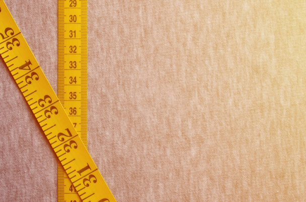 Il nastro di misurazione giallo con indicatori numerici sotto forma di centimetri o pollici si trova su un tessuto lavorato a maglia grigio. Concetto industria associata al cucito abbigliamento sportivo per specifiche dimensioni del corpo
 - Foto, immagini