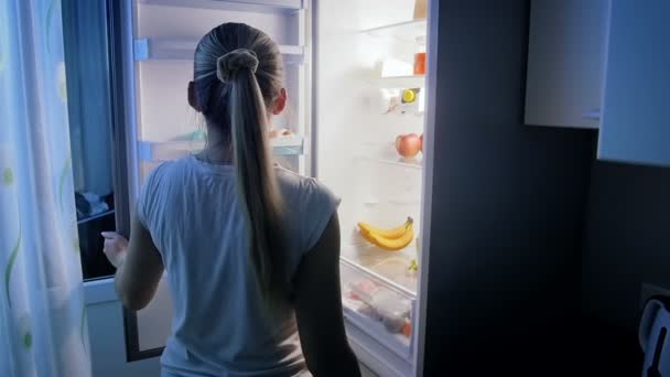 Αργή κίνηση βίντεο νεαρή γυναίκα που ψάχνει για τα τρόφιμα στο ψυγείο το βράδυ - Πλάνα, βίντεο