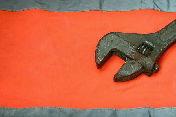 Регулируемый гаечный ключ на фоне оранжевой рубашки работника сигнализации. Натюрморт, связанный с ремонтом, железнодорожными или сантехническими работами
 - Фото, изображение