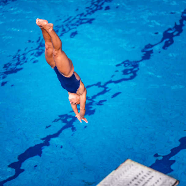 女性ダイバーが飛び込み台からプールに飛び込む - 写真・画像