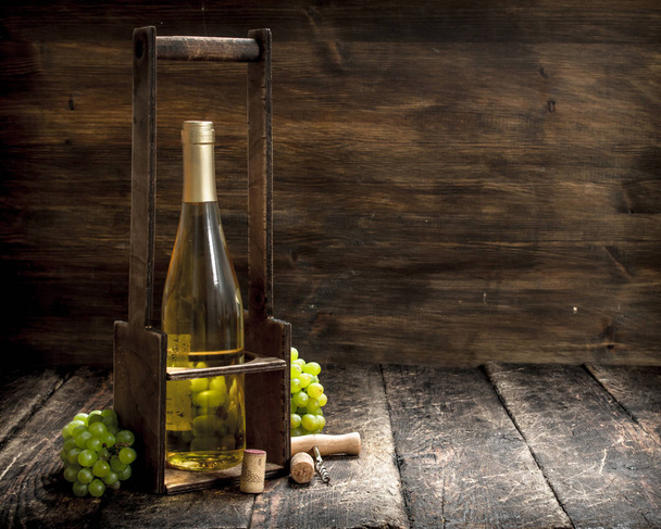 Víno na pozadí. Bílé víno na stojanu s větvemi čerstvých vinných hroznů. - Fotografie, Obrázek