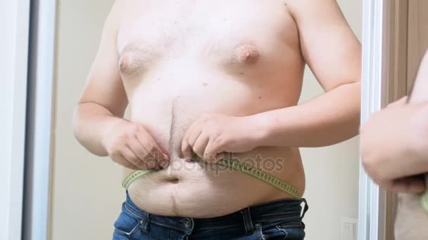 4 k video van overgewicht man probeert te meten zijn grote maag met geel meetlint op spiegel - Video
