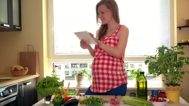 mujer embarazada feliz con la computadora de la PC tableta que prepara la ensalada vegetal en casa
 - Metraje, vídeo