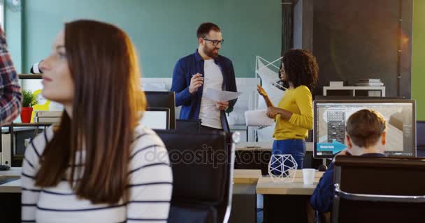 Young multi-ethnic coworkers talking and discussing a project on the background. Blurred female offfice worker on the front. modern comfortable office room. - Footage, Video