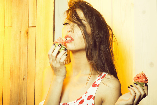 Closeup portret van een mooie sensuele jongedame met make-up houden van lekker verse huisgemaakte cup cakes met sinaasappel crème met bloem suikerglazuur in Groenboek indoor, horizontale foto - Foto, afbeelding