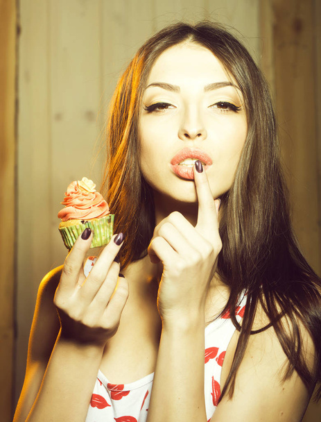Closeup view portrait of one beautiful sensual young woman with makeup holding tasty fresh homemade cup cake with orange cream with flower icing in green paper indoor, vertical photo - Foto, afbeelding