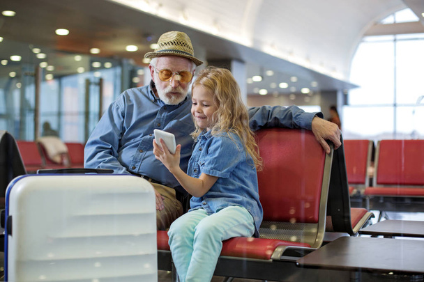 Cheerful little girl is holding smartphone with old man - Foto, afbeelding