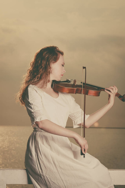 Женщина играет на скрипке рядом с пляжем
 - Фото, изображение