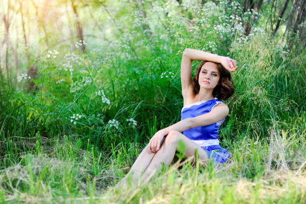 Young brunette girl in blue dress posing lying on grass in summer park - Photo, image