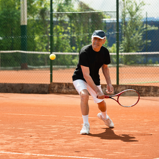 Homme âgé frappant balle sur le court de tennis
 - Photo, image