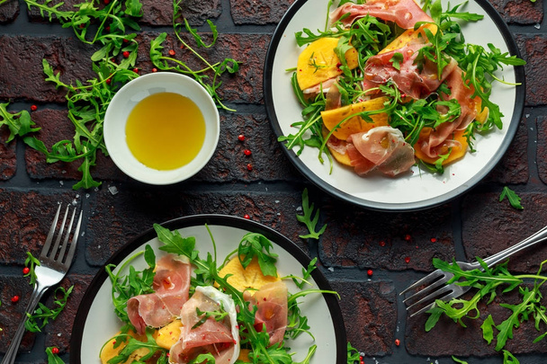 Fresh Tasty Persimmon salad with arugula, parma ham, olive oil and herbs. autumn, winter healthy food - Photo, image