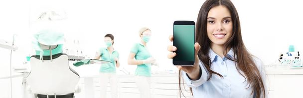 dental care smiling woman showing smart phone on dentist clinic  - Photo, Image
