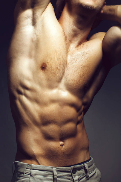 Seksikäs lihaksikas mies vartalo urheilija kehonrakentaja poseeraa vallassa suonet käsissä ja paljain rinnassa harmaalla taustalla
 - Valokuva, kuva