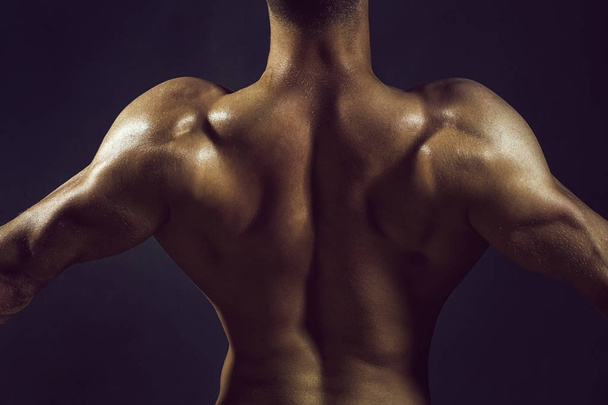 Sexy gespierde man achterkant atleet bodybuilder poseren in macht met opgeheven handen en kale romp op donkere achtergrond - Foto, afbeelding