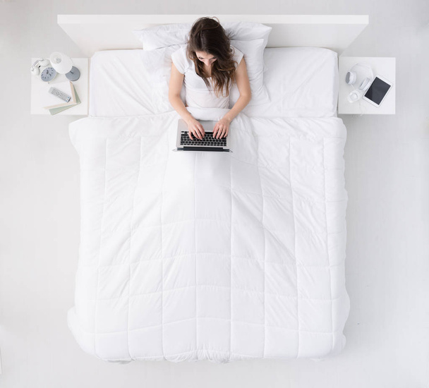 Woman using a laptop on her bed - Photo, image