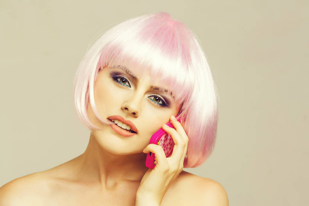 sexy glamour girl or woman with fashionable makeup on pretty face and short hairstyle or pink wig holding plastic toy mobile phone in studio on light background - Fotoğraf, Görsel