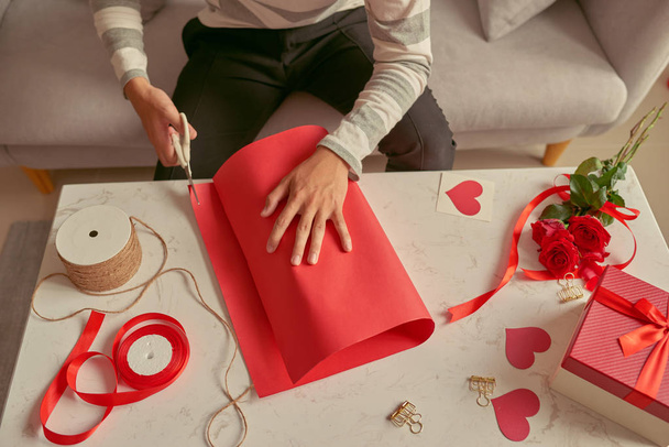 A man wrapping gifts  in red ribbon and fresh roses. Valentines concept - Fotoğraf, Görsel
