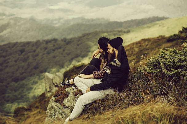 Man and girl hipster couple sit on slope covered with forest and green grass on summer vacation on mountain scene - Фото, зображення