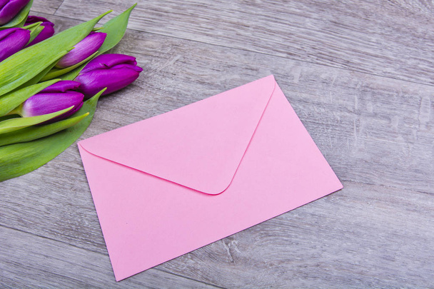 Розовый конверт с тюльпанами на столе
 - Фото, изображение