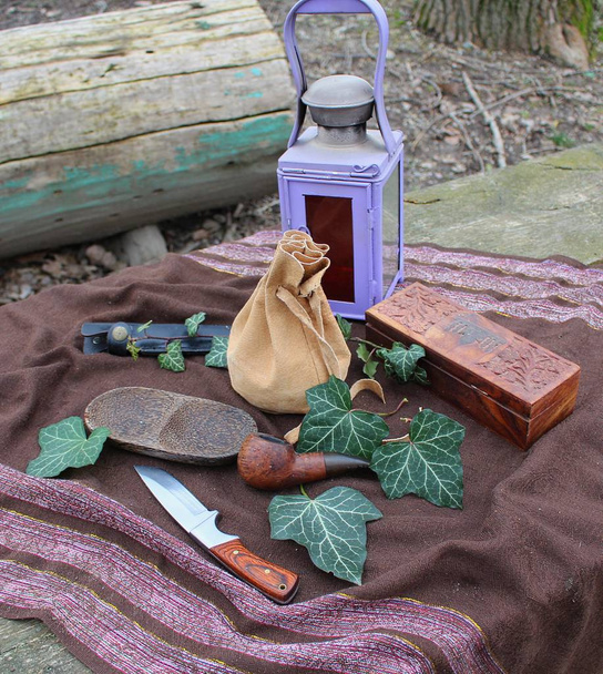 Still Life - a vintage lamp, knife, wooden pipe, box and a poach arranged on a table in a garden with ivy leaves - Photo, Image